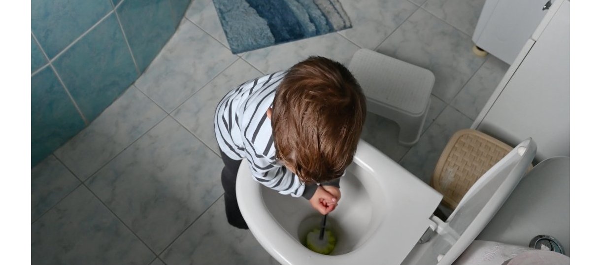 Toddler using a toilet brush to clean the toilet bowl