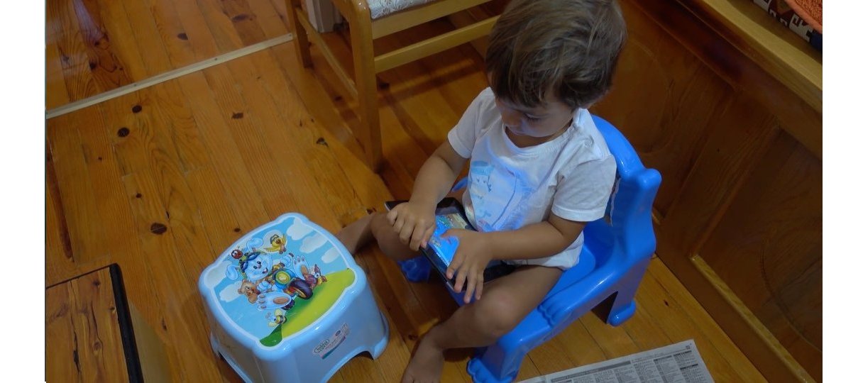 Toddler sitting on a potty while playing a game on a tablet