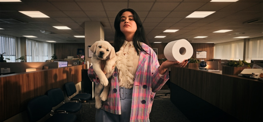 A woman in an office holding a toilet roll in the one hand and a puppy in the other arm
