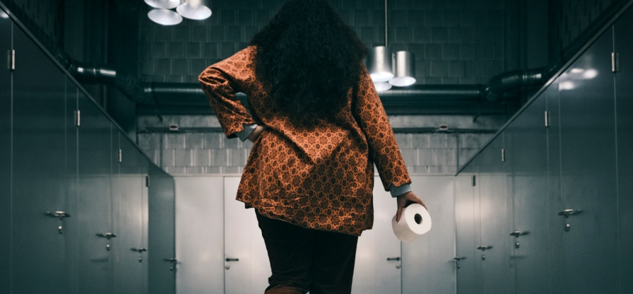 A woman with a roll of toilet paper walking towards toilet stalls