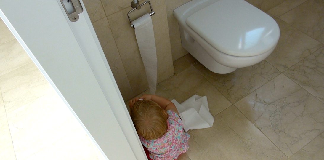 Child unrolling toilet paper on bathroom floor