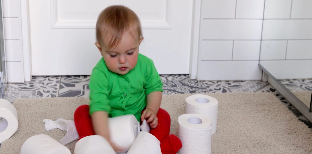 Child playing with toilet paper rolls on a bathroom floor