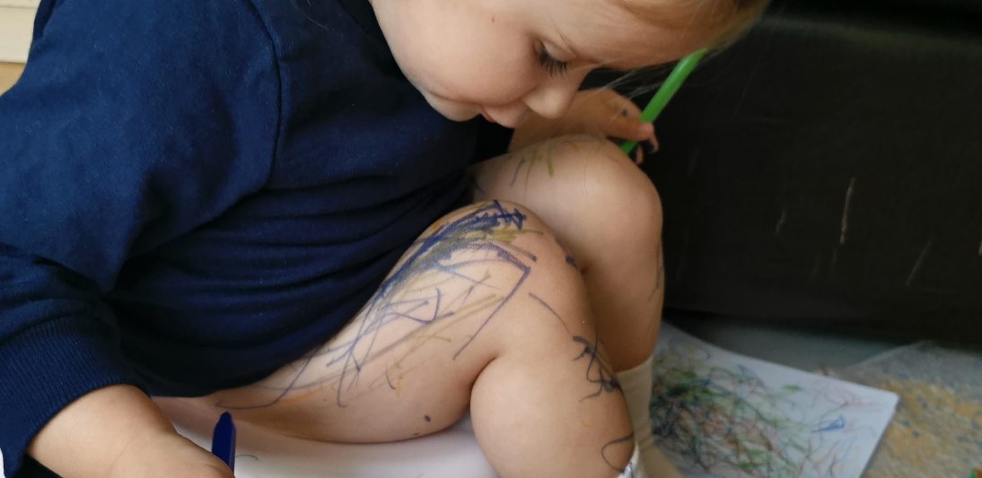Toddler sitting on a toilet drawing on her leg