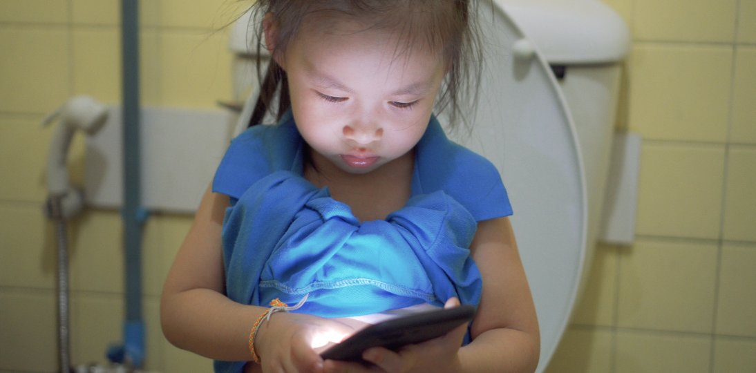 Child looking at a mobile phone while sitting on the toilet