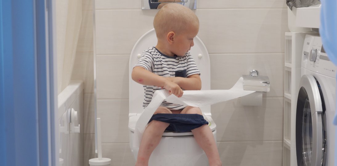 Child sitting on a toilet while unrolling toilet paper
