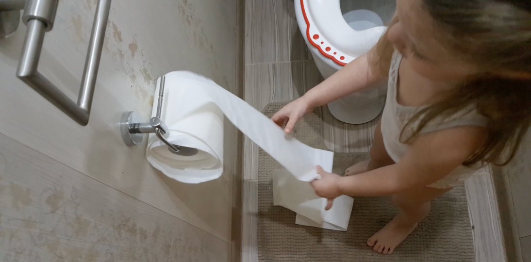 Child unrolling toilet paper in the bathroom