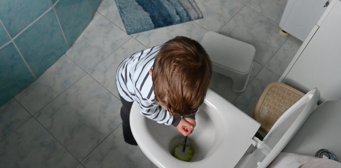 Child using a toilet brush to clean a toilet